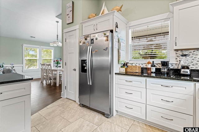 kitchen with dark stone countertops, stainless steel refrigerator with ice dispenser, decorative light fixtures, and white cabinets