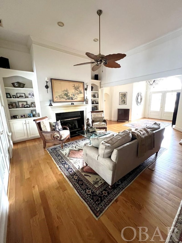 living room with light wood-type flooring, built in features, crown molding, and a glass covered fireplace