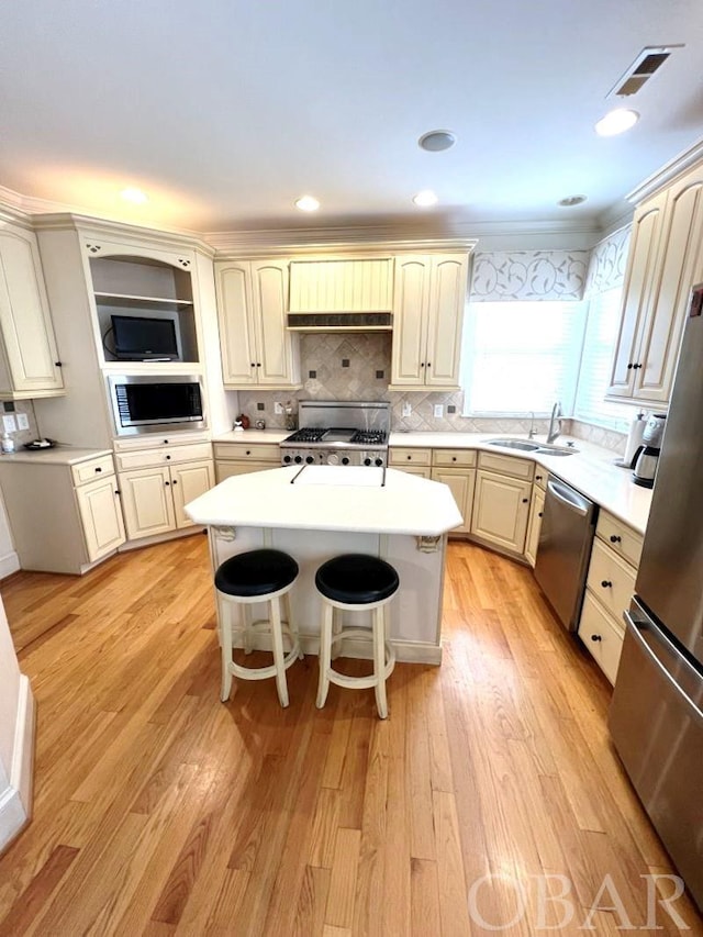 kitchen with appliances with stainless steel finishes, a breakfast bar, a center island, light countertops, and a sink