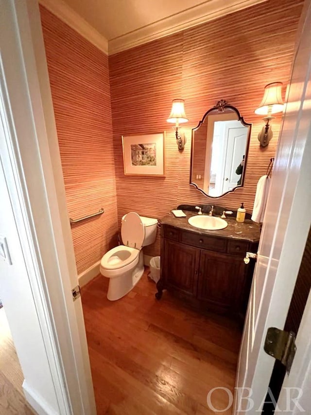 half bathroom with toilet, wood finished floors, vanity, baseboards, and crown molding