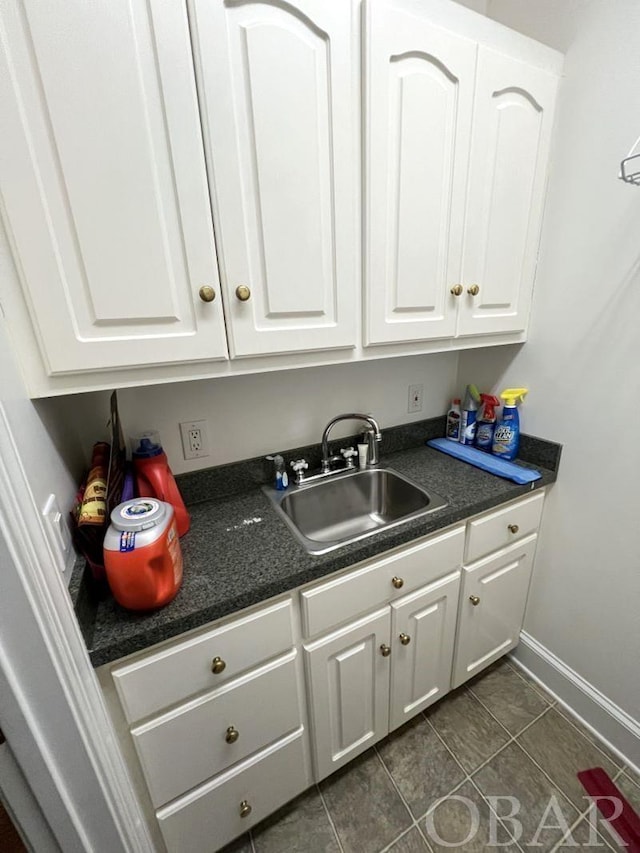 kitchen with dark countertops, white cabinets, a sink, dark tile patterned flooring, and baseboards