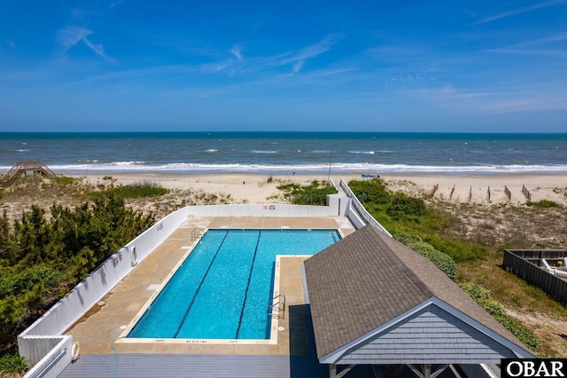 community pool with a beach view, a water view, and fence