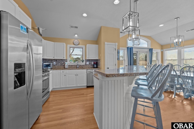 kitchen with white cabinets, a center island, hanging light fixtures, stainless steel appliances, and a kitchen bar