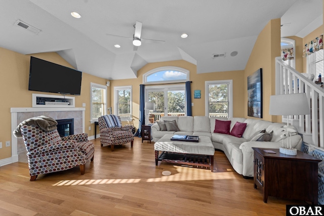 living room with vaulted ceiling, light wood finished floors, a tiled fireplace, and visible vents