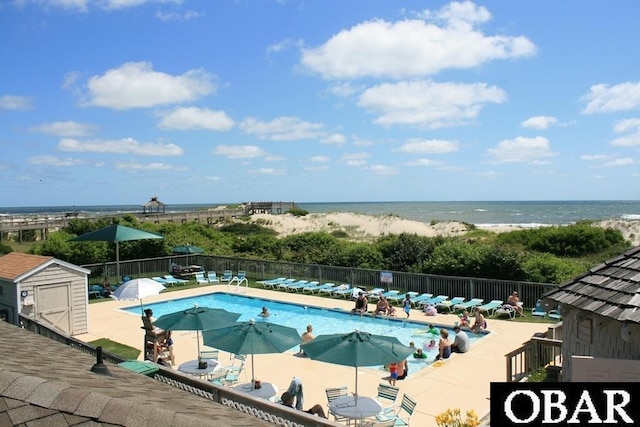 community pool featuring a water view, fence, a beach view, and a patio