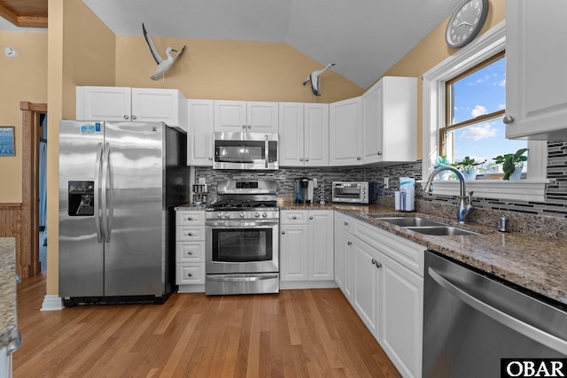 kitchen featuring lofted ceiling, stainless steel appliances, a sink, white cabinets, and dark stone counters