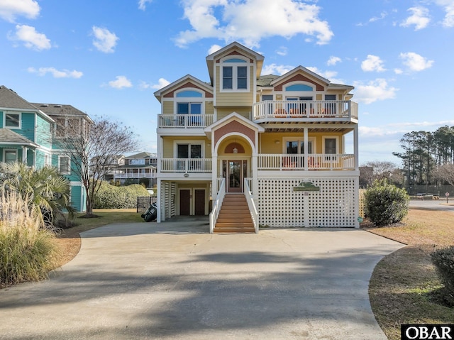 raised beach house with concrete driveway, stairway, an attached garage, and a balcony