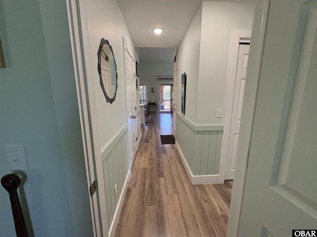 corridor featuring a wainscoted wall, a decorative wall, and light wood-style floors