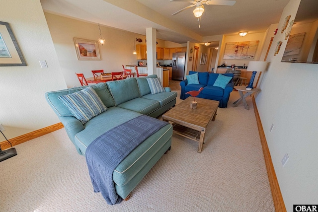 living area with a ceiling fan, light colored carpet, and baseboards