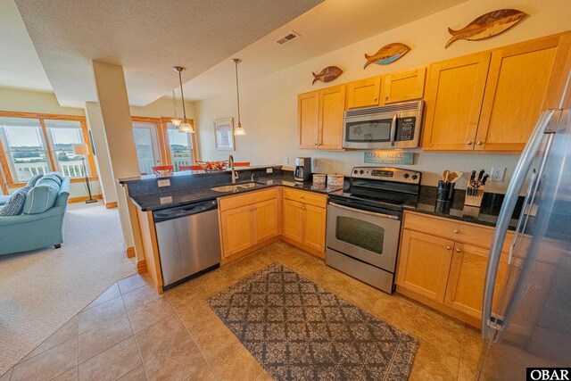 kitchen with stainless steel appliances, a peninsula, a sink, dark countertops, and decorative light fixtures