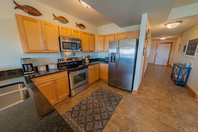 kitchen featuring light brown cabinets, appliances with stainless steel finishes, a sink, and baseboards