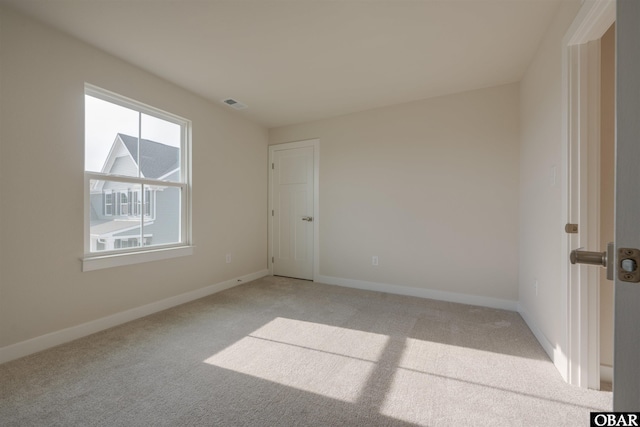 empty room featuring visible vents, light carpet, and baseboards