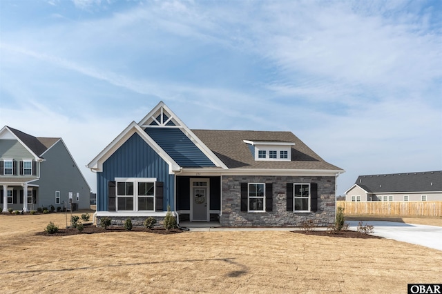 craftsman-style house featuring board and batten siding, stone siding, roof with shingles, and fence