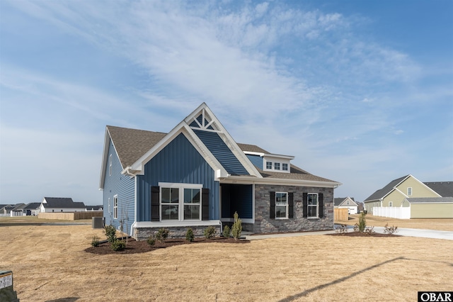 craftsman-style home featuring stone siding, central AC unit, board and batten siding, and fence