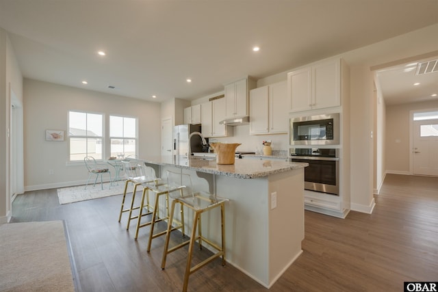 kitchen featuring under cabinet range hood, stainless steel appliances, visible vents, dark wood finished floors, and a center island with sink