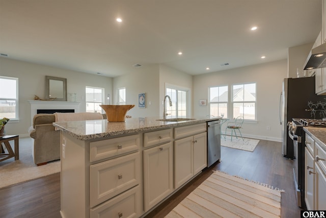 kitchen with electric range oven, an island with sink, stainless steel dishwasher, white cabinetry, and a sink