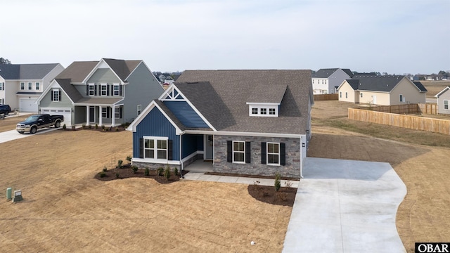 craftsman-style house with fence, stone siding, concrete driveway, a residential view, and board and batten siding