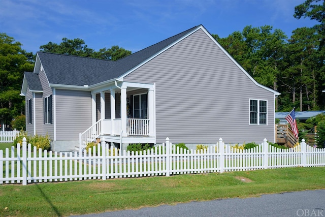 view of side of property featuring a fenced front yard, a lawn, and roof with shingles