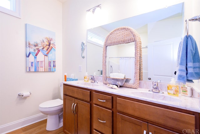 bathroom featuring double vanity, wood finished floors, a sink, and toilet