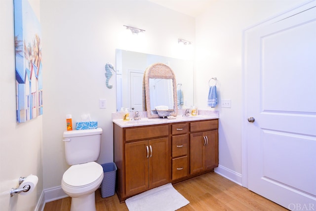 full bathroom with toilet, double vanity, a sink, and wood finished floors