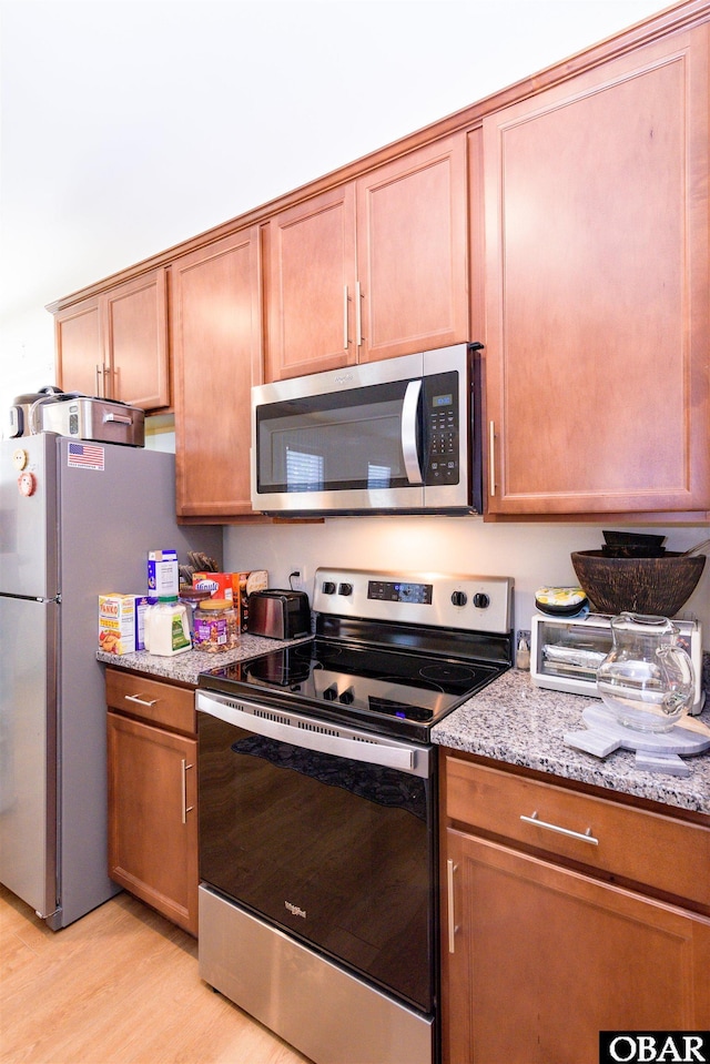 kitchen featuring stainless steel appliances, light wood-style flooring, and light stone countertops