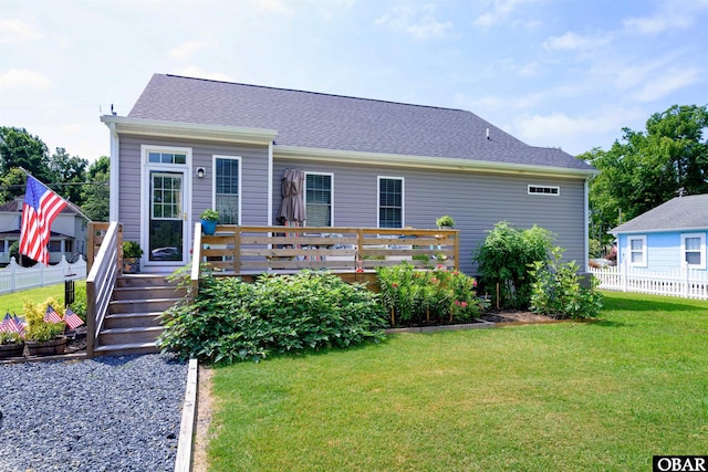 view of front facade featuring a shingled roof, a deck, fence, and a front lawn