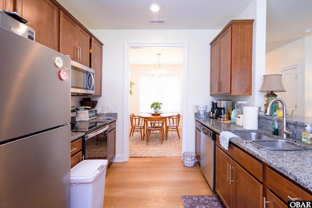 kitchen with appliances with stainless steel finishes, stone countertops, brown cabinets, and a sink