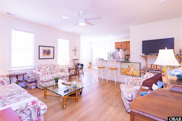 living room featuring light wood-style floors, visible vents, and ceiling fan