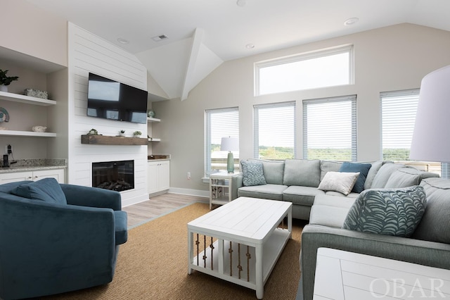 living area featuring lofted ceiling, built in shelves, a large fireplace, visible vents, and light wood-style floors