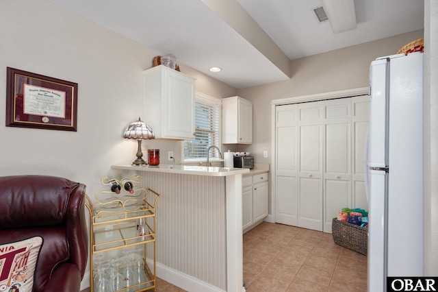 kitchen with light tile patterned floors, freestanding refrigerator, a sink, light countertops, and white cabinets