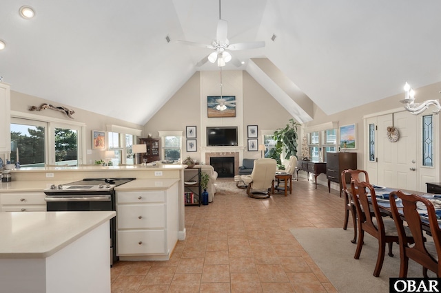 kitchen with stainless steel range with electric stovetop, a ceiling fan, white cabinetry, a fireplace, and light countertops