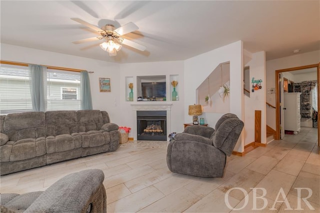 living area with ceiling fan, a fireplace, baseboards, and light wood-style floors