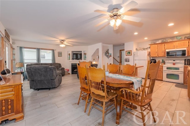 dining room with light wood-style flooring, a fireplace, ceiling fan, and recessed lighting