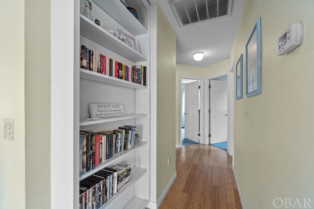 hallway featuring visible vents, baseboards, and wood finished floors