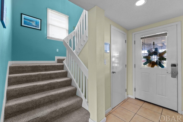 foyer entrance with stairway, a textured ceiling, and light tile patterned flooring