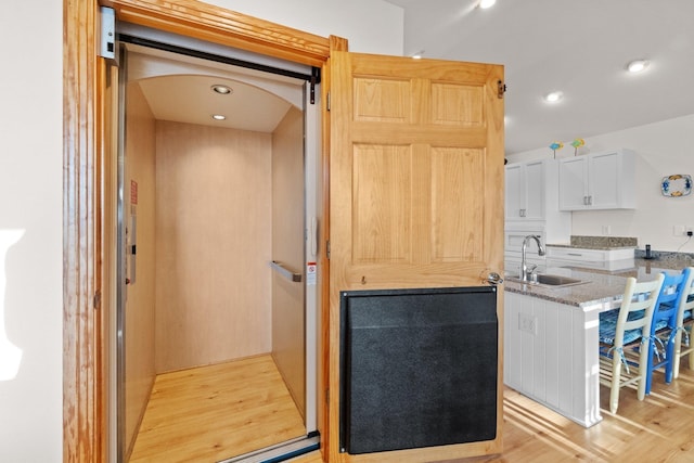 kitchen with recessed lighting, a sink, white cabinetry, light wood-style floors, and elevator