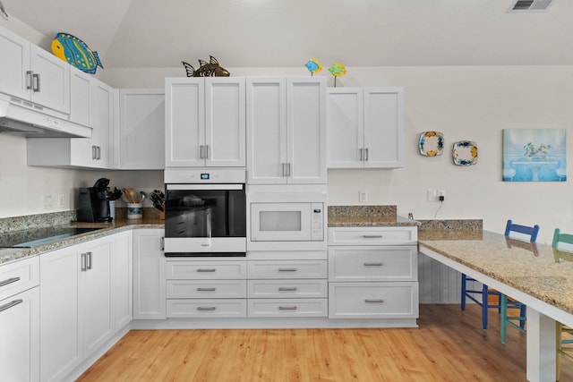 kitchen with light wood finished floors, white microwave, oven, under cabinet range hood, and black electric cooktop