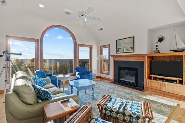 living area featuring high vaulted ceiling, a fireplace with flush hearth, wood finished floors, visible vents, and a ceiling fan