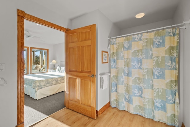 ensuite bathroom with ensuite bathroom, ceiling fan, curtained shower, wood finished floors, and baseboards