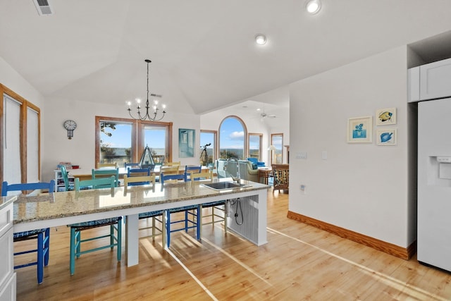 kitchen with white refrigerator with ice dispenser, visible vents, white cabinets, vaulted ceiling, and a kitchen breakfast bar