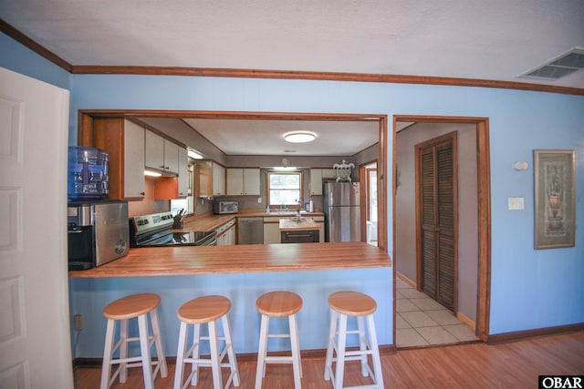kitchen with stainless steel appliances, light wood-type flooring, visible vents, a peninsula, and light countertops