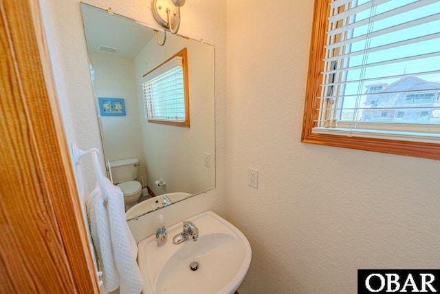 half bathroom featuring toilet, visible vents, a sink, and a textured wall