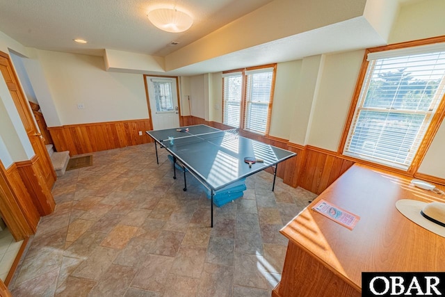 game room featuring vaulted ceiling, a wainscoted wall, wood walls, and a textured ceiling