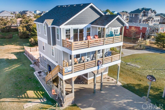 rear view of house featuring a shingled roof, concrete driveway, board and batten siding, a balcony, and a residential view