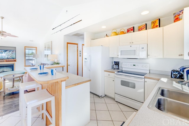 kitchen with a breakfast bar area, light countertops, vaulted ceiling, a sink, and white appliances