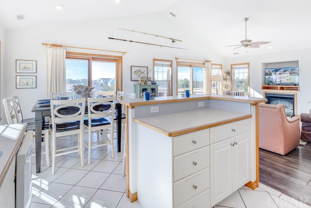 kitchen with light countertops, a glass covered fireplace, open floor plan, and white cabinetry