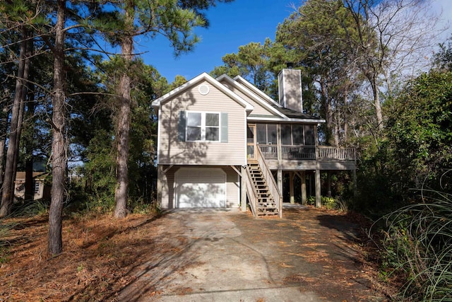 exterior space featuring a chimney, a sunroom, a garage, driveway, and stairs