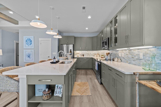 kitchen featuring a center island with sink, stainless steel appliances, tasteful backsplash, gray cabinets, and hanging light fixtures