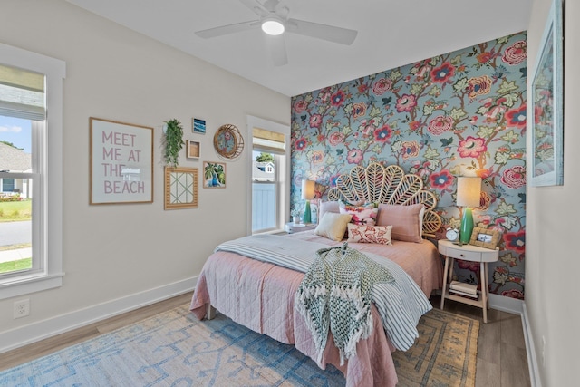 bedroom with a ceiling fan, multiple windows, baseboards, and wood finished floors