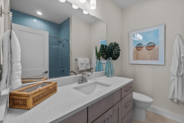 bathroom featuring tile patterned flooring, toilet, vanity, baseboards, and a tile shower